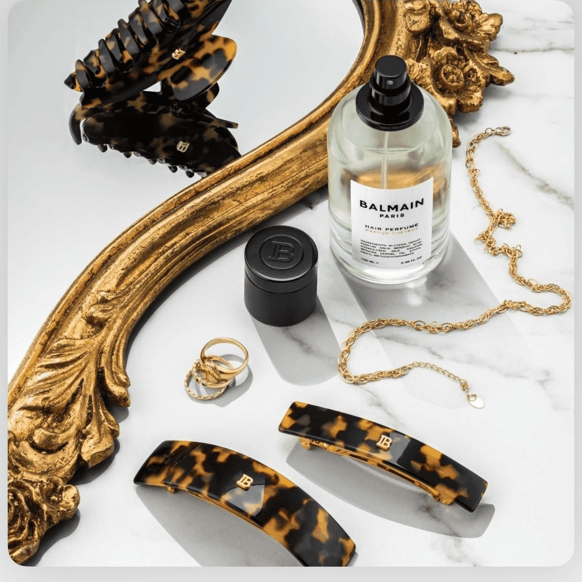 Tortoiseshell hair clips and jewelry on marble with Balmain hair perfume and gold mirror.