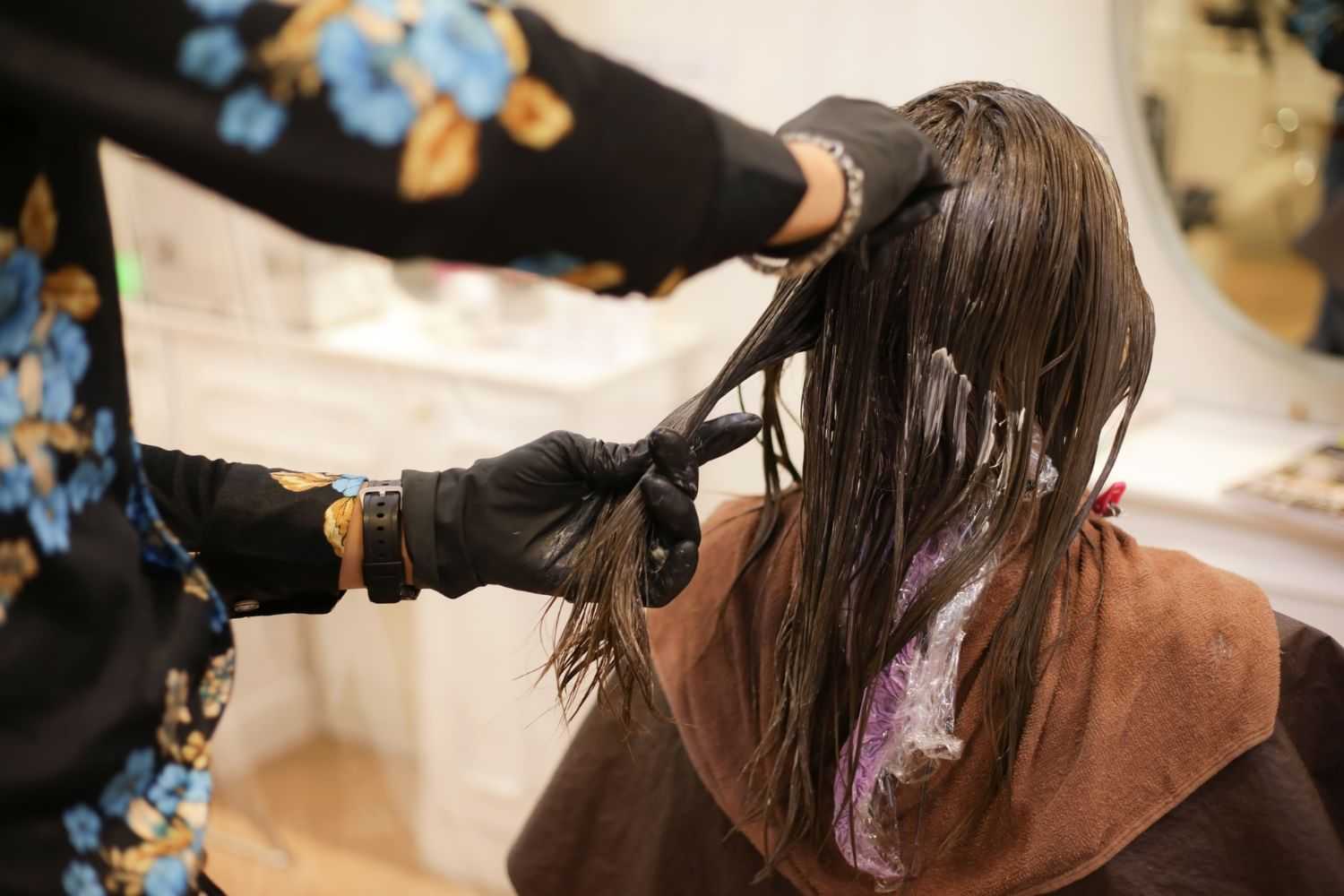 Hairdresser applying treatment to client's wet hair in a salon.