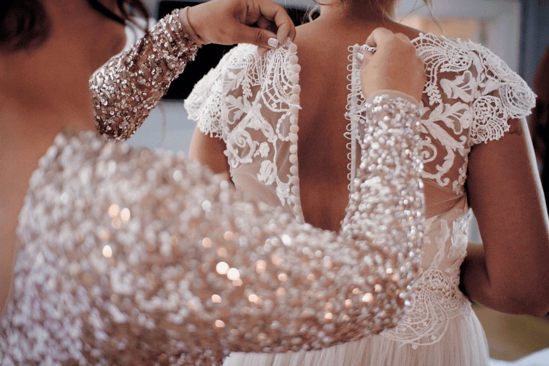 Bridesmaid helping bride with intricate lace gown fastening.